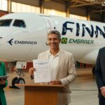 Três executivos em hangar com avião Embraer Finnair ao fundo durante cerimônia de assinatura de contrato aeronáutico