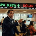 Homem de terno aponta para painel eletrônico mostrando Ibovespa em alta de 0,78% e dólar em queda de 1,13% em pregão da bolsa