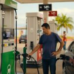 Homem abastecendo veículo em posto de combustível com bomba de etanol, preços visíveis no display eletrônico