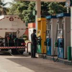 Caminhão-tanque branco abastecendo posto de gasolina com múltiplas bombas de combustível, mercado de distribuição