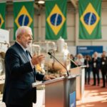 Presidente Lula em discurso oficial com bandeiras brasileiras ao fundo e equipamentos industriais, biocombustíveis
