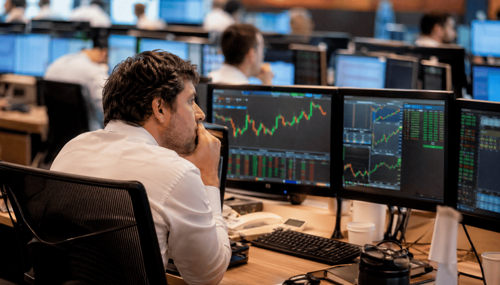 Trader concentrado observando múltiplos monitores com gráficos financeiros e cotações em tempo real no pregão