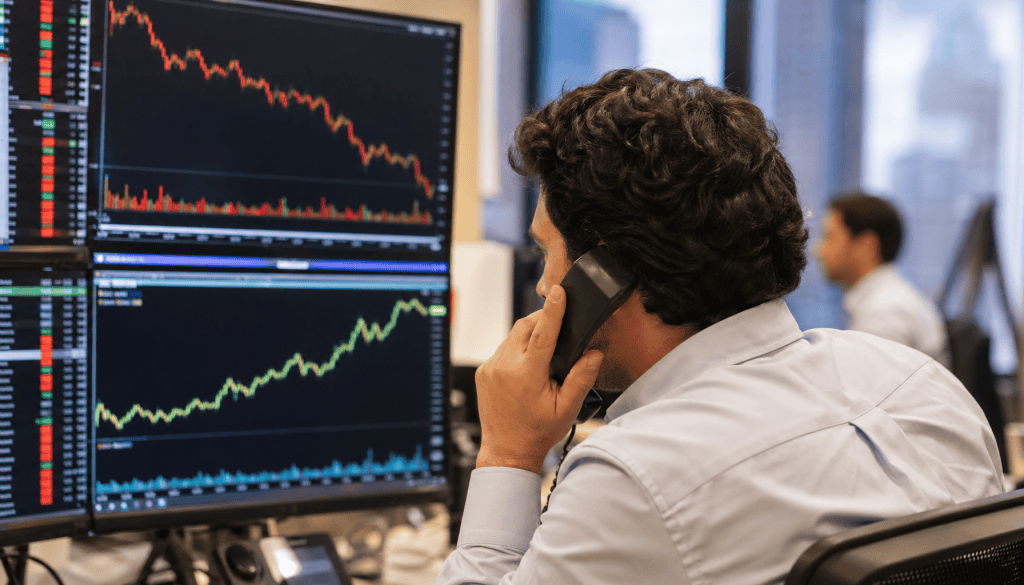 Trader ao telefone observando monitores com gráficos financeiros em queda, indicadores vermelhos e verdes, mercado ações Ibovespa