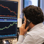 Trader ao telefone observando monitores com gráficos financeiros em queda, indicadores vermelhos e verdes, mercado ações Ibovespa