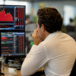 Trader de costas observando múltiplos monitores com gráficos vermelhos de queda no mercado financeiro, bolsa de valores
