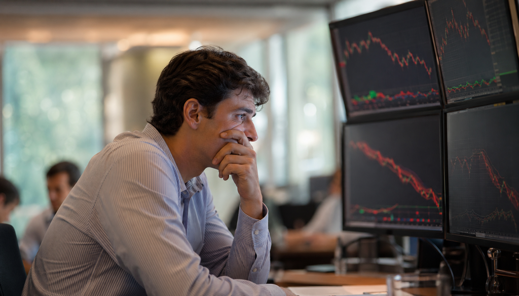 Trader concentrado observando monitores com gráficos financeiros em queda, indicadores vermelhos, análise técnica bolsa