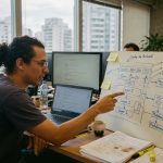 Desenvolvedor trabalhando em diagrama de arquitetura blockchain com computadores em escritório, tecnologia financeira