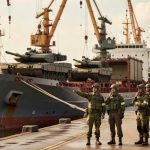 Soldados militares em formação ao lado de navio cargueiro com tanques de guerra em porto comercial infraestrutura defesa